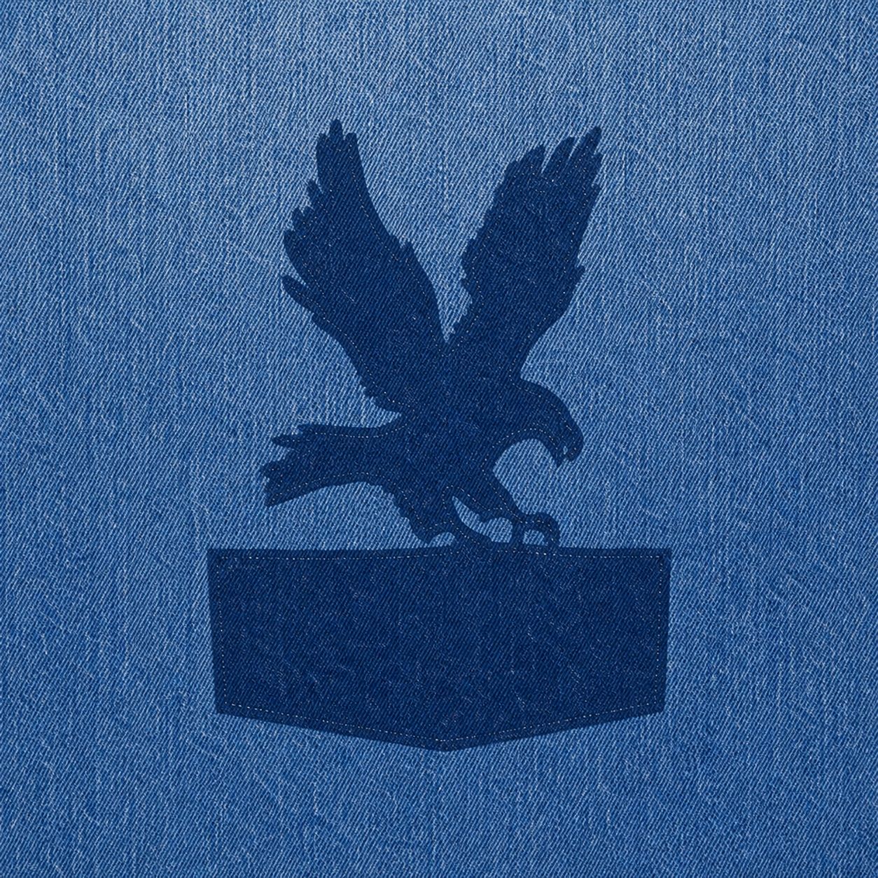 Unfaded eagle-and-pocket patch shape with needle holes in the sun-faded denim, center back, macro.
