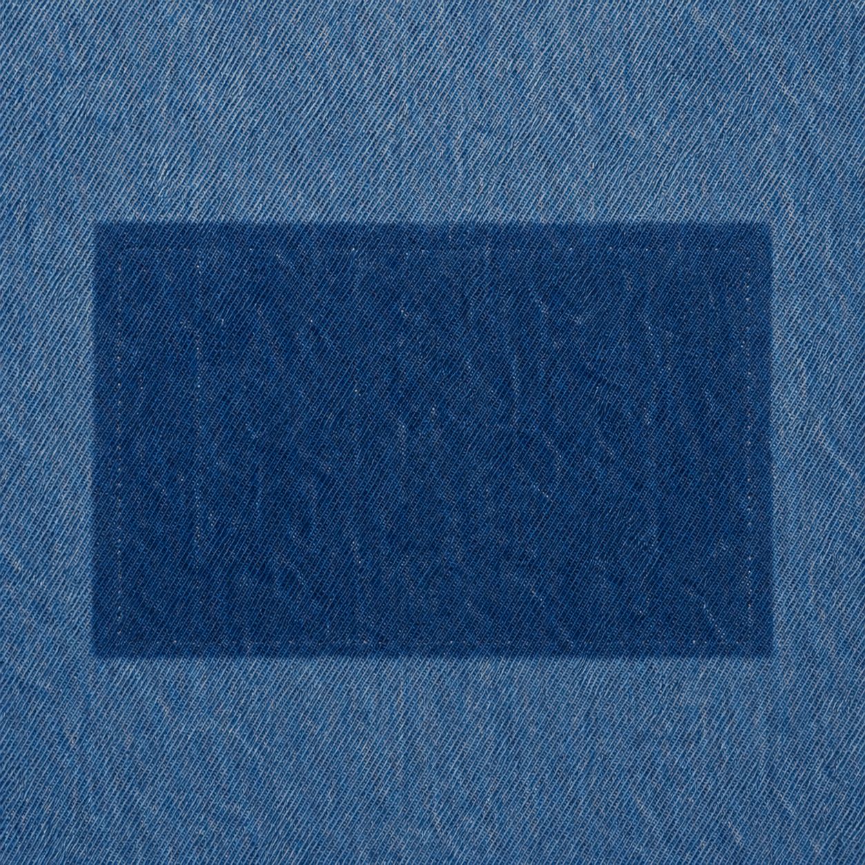 Unfaded patch-shaped area with needle holes in the sun-faded denim, chest, macro.