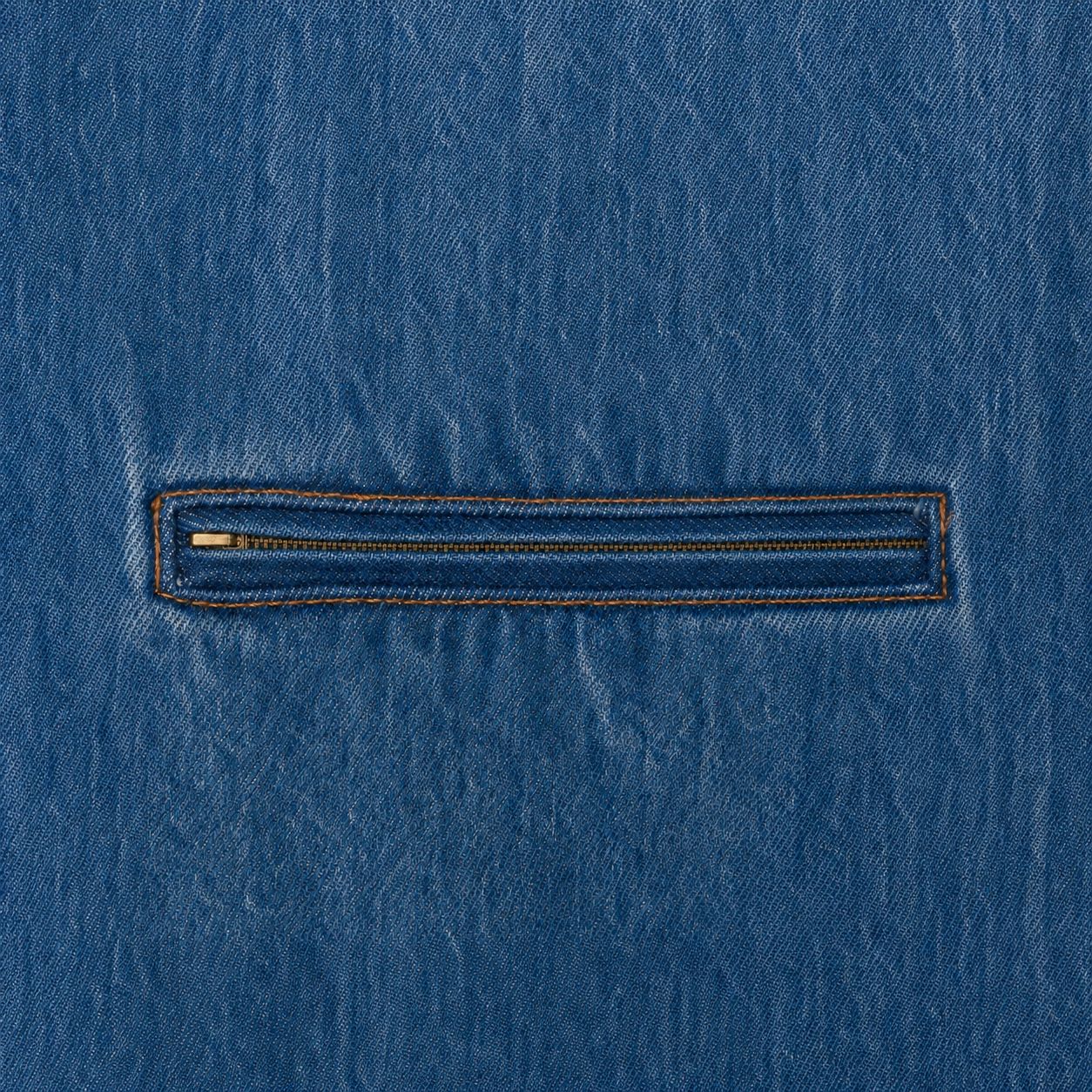 Zippered chest pocket detail, antique brass zip in washed denim, macro.