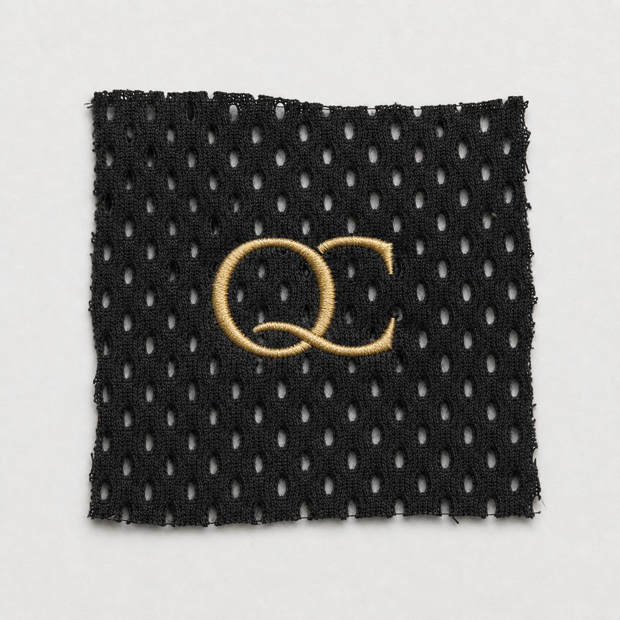 Metallic gold QC logo embroidery sample on black athletic mesh.