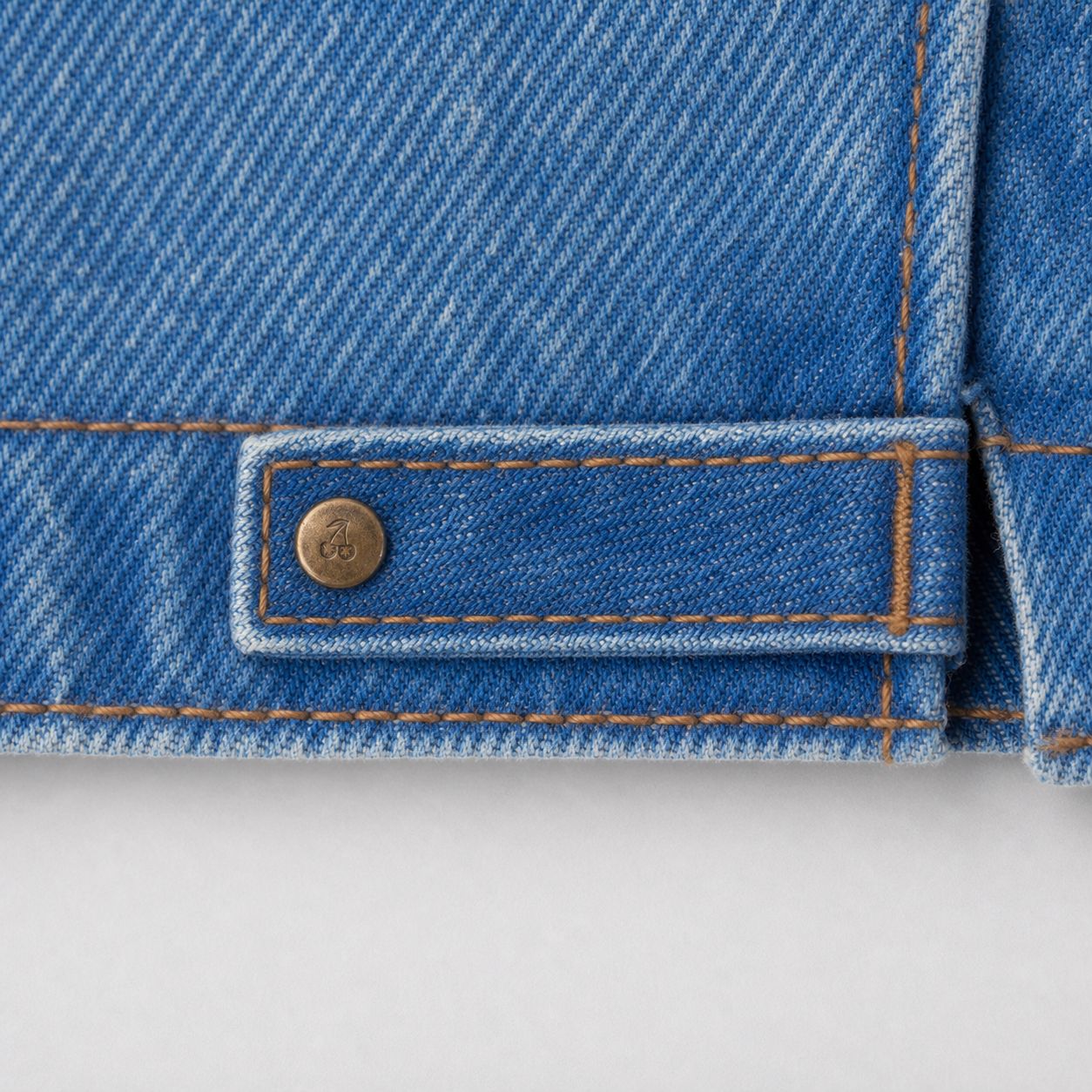 Custom cherry-marked rivet at the hem opening, macro.