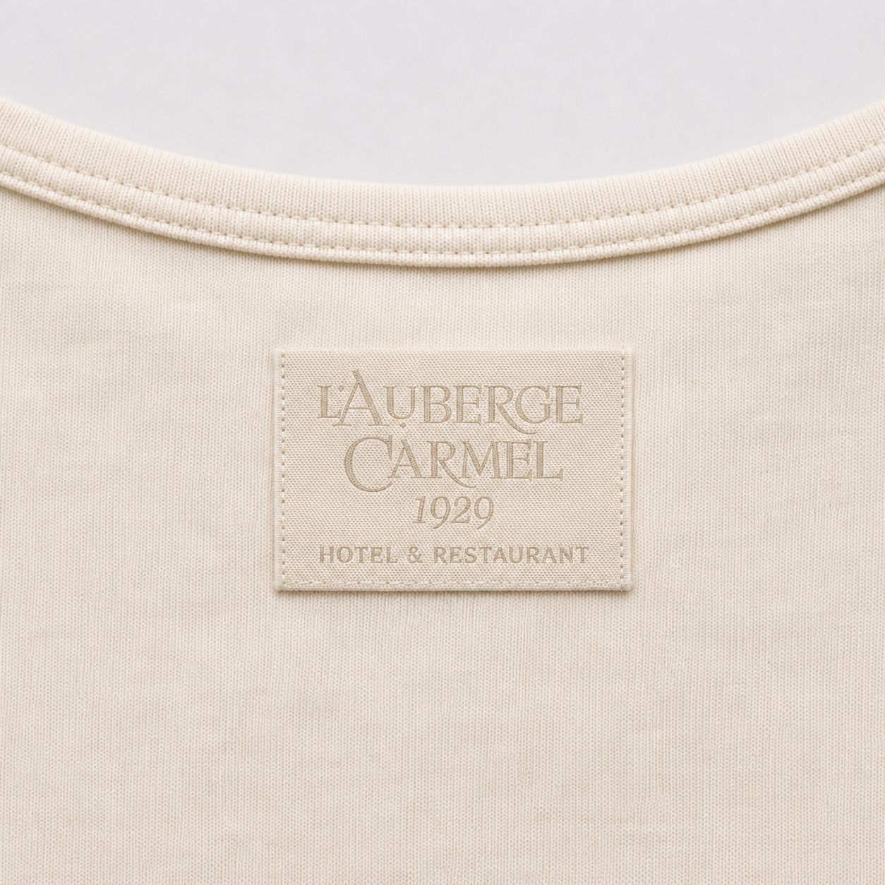 Tone-on-tone woven L'Auberge Carmel 1929 Hotel & Restaurant label at the upper back, below the neckline, macro.